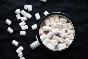 Cup of cocoa with marshmallows on a black background where white marshmallows are scattered