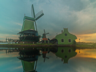 Traditional Dutch windmill and house reflected in the calm waters of Zaanse Schans at sunset