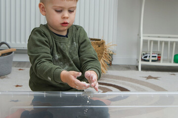 Toddler kid playing with homemade kinetic sand in a plastic box at home