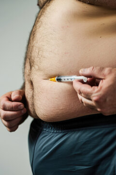Fat man holding a syringe with a blood sample on his stomach. Conceptual photo of diabetes/slimming injection.