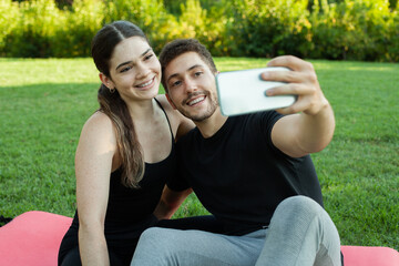 Pareja heterosexual caucasica enamorados haciendose un selfie en el cesped del parque posando...