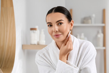 Beautiful woman removing makeup with cotton pad indoors