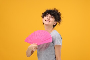Happy woman holding hand fan on orange background