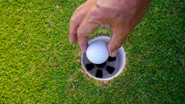 Hand holding golf ball out of golf hole.