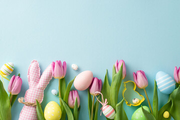 Family Easter setup. Top view of lively eggs, playful cookie cutter, charming bunny, and tulips against a pastel blue background. Ample space for text or promotions