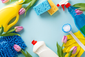 Spring freshness with cleaning essentials. Overhead shot of dusters, scrubbers, gloves, flowers and detergents on a soft blue backdrop. Ideal for promotional messages or ads