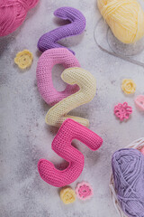 New Years background 2025. Multicolored crochet numbers, skein of wool yarn and knitting needles on gray background. New Years start creative handcrafted idea for DIY crafters