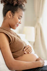 Joyful multiracial pregnant woman looking at her stomach expecting for childbirth. Young beautiful expectant mother relaxing on bed at home. Pregnancy and motherhood feminine anticipation lifestyle.