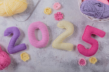 New Years background 2025. Multicolored crochet numbers, skein of wool yarn and knitting needles on...