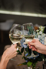 Couple in love drinking white wine. Cheers. Romantic date by candlelight at night. Hands man and woman hold glasses at home. Toast. Dinner setup table for couple on Valentine's day. Closeup.