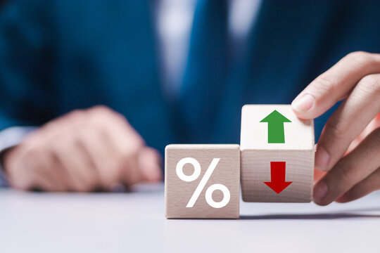 Business and finance concept. Businessman holding wooden block with percent and up or down arrow icon for mortgage and loan rates. Interest rate, stocks, ranking.