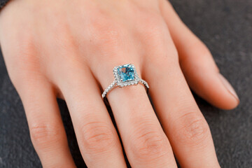 Beautiful female hand with gold ring with diamonds and aquamarine on gray background