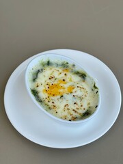 Baked spinach with cheese in a white cup on white backaround.