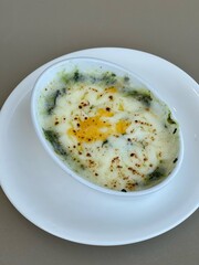 Baked spinach with cheese in a white cup on white backaround.