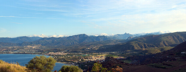 Panoramic aerial landscape view of Tindary at sunny autumn day. City on the shore of The Mediterranean Sea. Majestic mountains in the background. Travel and tourism concept