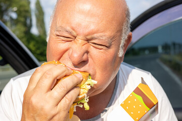 Grown man enjoying burger by the side of a car. The concept of fast food and takeaway food. Big juicy burger with cheese from McDonalds in the hand. Kiev, Ukraine, July 08 2023