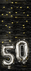 Silver foil balloon number 50 on a background of black tinsel with gold confetti. Birthday card, inscription fiftieth. Anniversary event. Vertical banner.