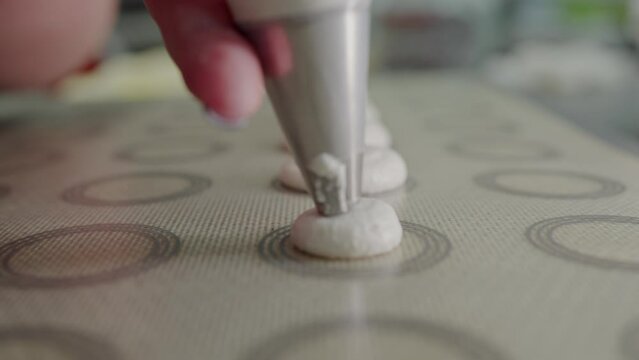 Closeup on woman hand with pastry piping bag squeezing out dough on tray for making coockies at home kitchen. Cooking macaroon process. Preparing homemade sweets