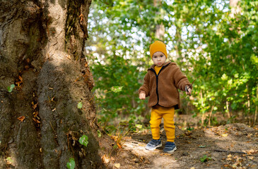 Little Boy in Brown Jacket and Yellow Pants Standing Next to a Tree