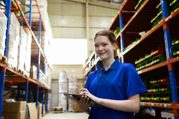 Female worker wearing safety uniform and hard hat using tablet checking inspect goods on shelves in warehouse. women worker check stock inspecting product in factory.