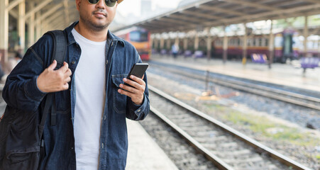 Man traveler waiting on station waiting for a train while using a smartphone. Backpacker male plan route of stop railway. Railroad transport and booked. The concept of a man traveling alone.
