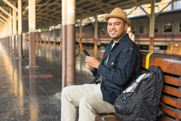 Man traveler waiting on station waiting for a train while using a smartphone. Backpacker male plan route of stop railway. Railroad transport and booked. The concept of a man traveling alone.