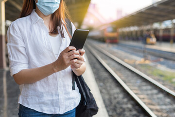 Woman traveler waiting on station waiting for a train while using a smartphone. Backpacker female plan route of stop railway. Railroad transport and booked. The concept of a woman traveling alone.