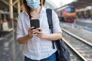 Woman traveler waiting on station waiting for a train while using a smartphone. Backpacker female plan route of stop railway. Railroad transport and booked. The concept of a woman traveling alone.