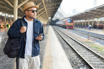 Man traveler waiting on station waiting for a train while using a smartphone. Backpacker male plan route of stop railway. Railroad transport and booked. The concept of a man traveling alone.