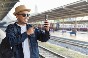 Man traveler waiting on station waiting for a train while using a smartphone. Backpacker male plan route of stop railway. Railroad transport and booked. The concept of a man traveling alone.