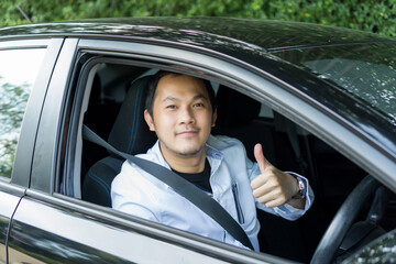 Happy male driver smiling while sitting in a car show thumbs up. Young asian man smile and looking through window. View of a Young man driving his car to travel on his holiday vacation time.