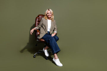Full length photo of confident business lady sitting on leather armchair for bosses enjoying workplace isolated over khaki color background