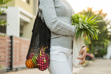 Woman hands holding shopping bag fruits and vegetables on the way home. Reusable cotton and mesh eco bags for shopping. Set zero waste plastic free concept. Sustainable lifestyle concept.