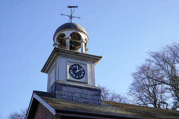 Small clock tower on roof of building. time piece and weather vane 