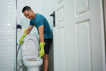 asian male wearing gloves cleaning toilet bowl in lavatory - obrazy, fototapety, plakaty