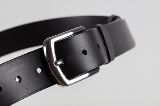 Part of a black leather classic belt with a buckle on a gray background.