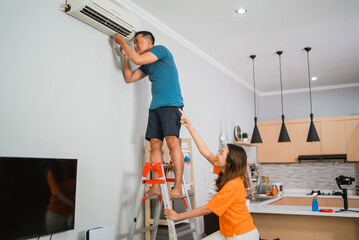 asian couple repair broken airconditioner together in the living room