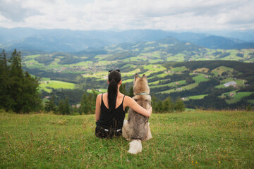young woman and siberian husky dog sitting hugging on an alpine mountain top in the summer