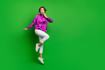 Full size photo of impressed crazy girl jumping unbelievable news empty space isolated on green color background