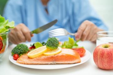 Asian elderly woman patient eating salmon steak breakfast with vegetable healthy food in hospital.