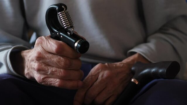 A seated pensioner trains his arms with a wrist expander. recovery of an old man after a stroke and heart attack, hand training. active lifestyle of a pensioner