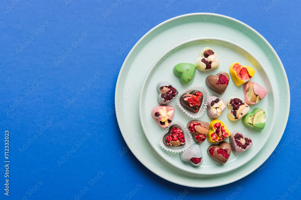 Poster Plate with different chocolate on colored background. Assortment of fine chocolates top view vith copy space Health and obesity concept