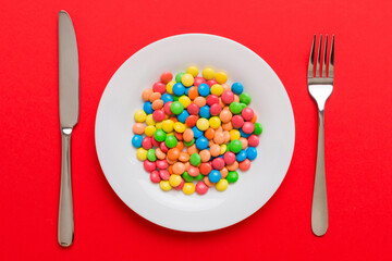 cutlery on table and sweet plate of candy. Health and obesity concept, top view on colored...