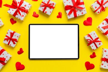 Fototapeta na wymiar Top view of digital tablet with gift boxes and hearts on colorful background. Tablet with black screen with Holiday decorations gift box top view