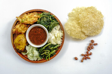 Pecel or pecal is traditional Javanese salad with peanut sauce. Served on a wooden plate with bakwan or vegetable fritters and fried chicken isolated on white background