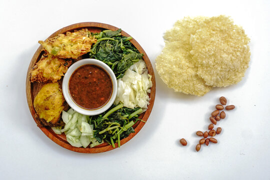Pecel or pecal is traditional Javanese salad with peanut sauce. Served on a wooden plate with bakwan or vegetable fritters and fried chicken isolated on white background
