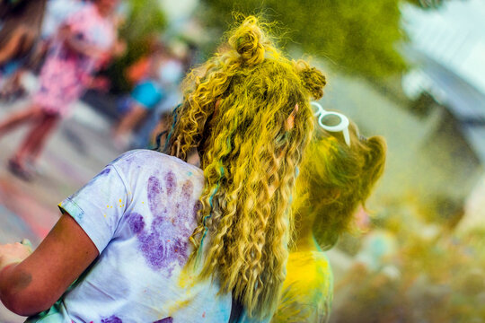 Girl covered in yellow paint with braids and wavy hair close-up at Holi festival
