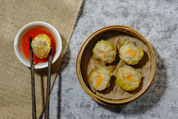 Steamed Dumpling Siew Mai served in a bamboo basket steamer with dipping sauce isolated on grey...