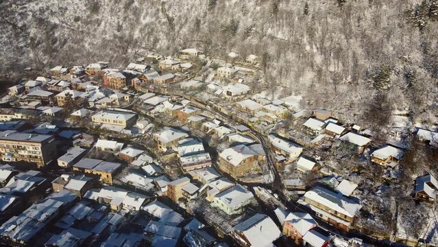 Borjomi Georgia winter 2024. private development scheme on the mountainside. roofs covered in snow, sunny weather. drone view moving forward, tilting the camera down. narrow streets of Georgia