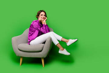 Full body length photo of cute cheerful business woman touching cheeks sitting in comfortable armchair isolated on green color background - obrazy, fototapety, plakaty